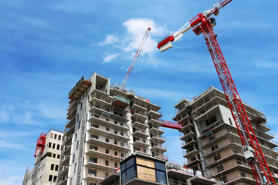 View of top of high-rise apartment building under construction with red and white cranes